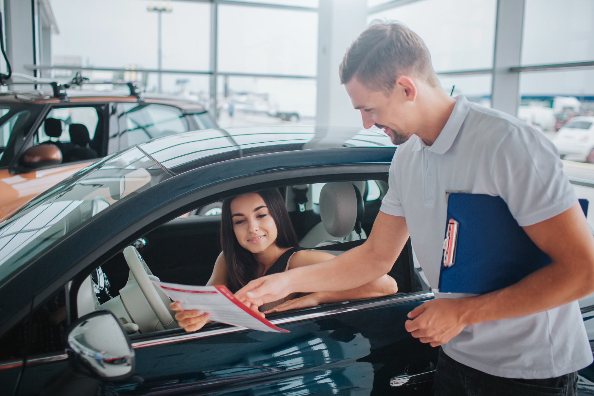 A woman signs paperwork from behind the wheel of her new vehicle